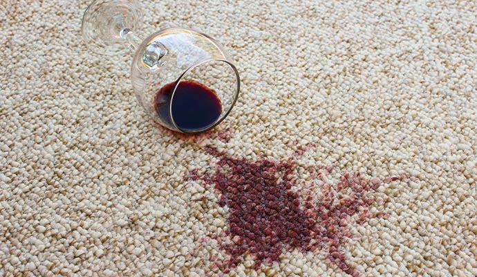 A glass of red wine spilled on a light-colored berber carpet
