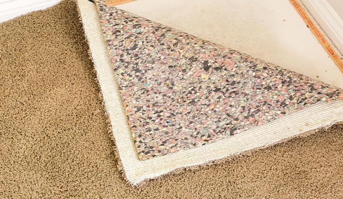 A corner of a brown residential carpet pulled back to show the underlying multi-colored recycled foam carpet padding