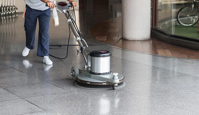 A professional technician using a high-speed rotary floor polisher on a grey granite floor