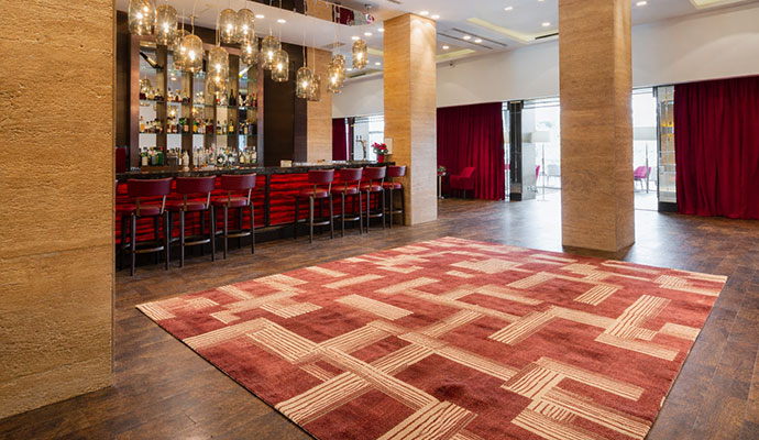 A large, patterned red area rug in a luxury hotel bar area with clean stone pillars and modern lighting.