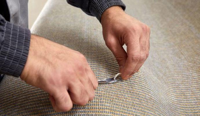 Close-up of a technician's hands carefully repairing a snagged carpet fiber to restore a smooth surface.
