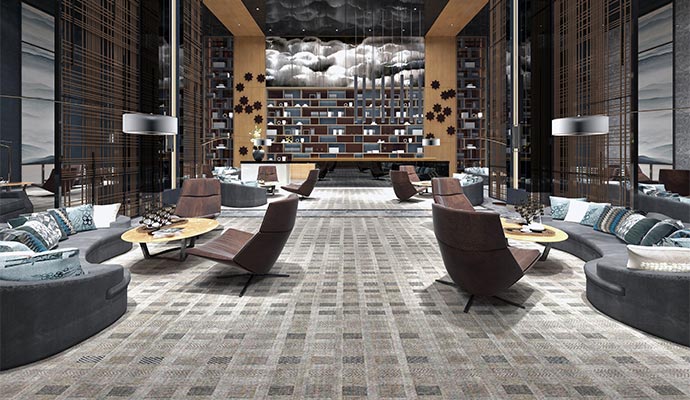 A spacious luxury lounge with grey patterned carpet, curved charcoal sofas, and brown leather accent chairs