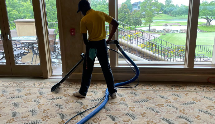 A professional cleaner using advanced equipment to deep clean a carpeted area inside a commercial property with large windows.