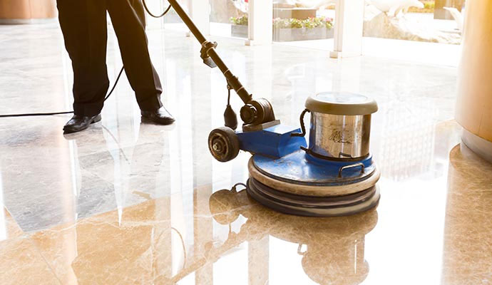 A technician using a high-speed floor buffer to restore the mirror-like shine of a luxury marble lobby floor.