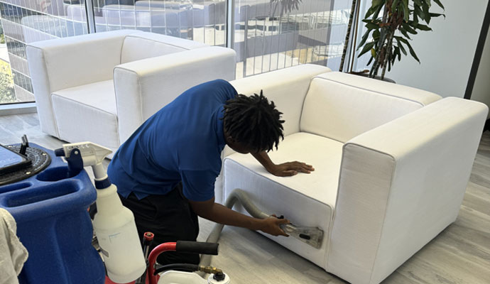A professional cleaner using specialized equipment to deep clean a white upholstered sofa in a modern space.