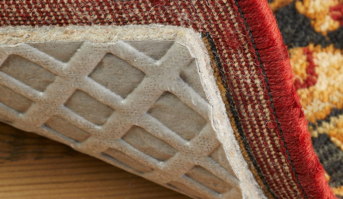 A close-up view of a rug pad beneath an area rug, showing added cushioning and fiber protection.