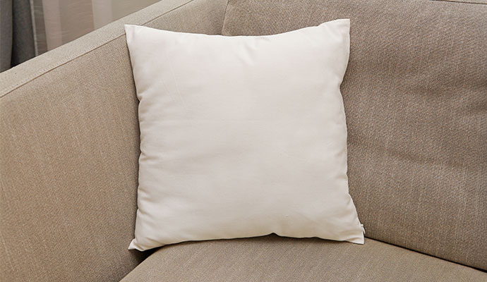 A single white throw pillow on a beige sofa showing the results of professional cleaning and protection.