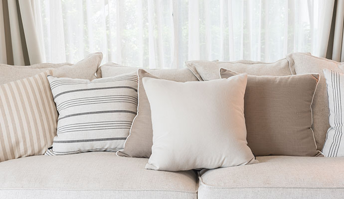 A set of clean, renewed decorative throw pillows in various neutral tones and patterns on a living room sofa.
