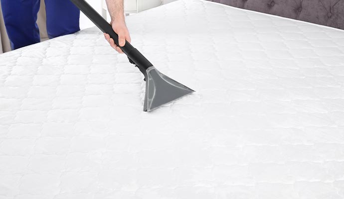 A professional cleaner using a specialized steam cleaning wand to sanitize and deep clean a white quilted mattress