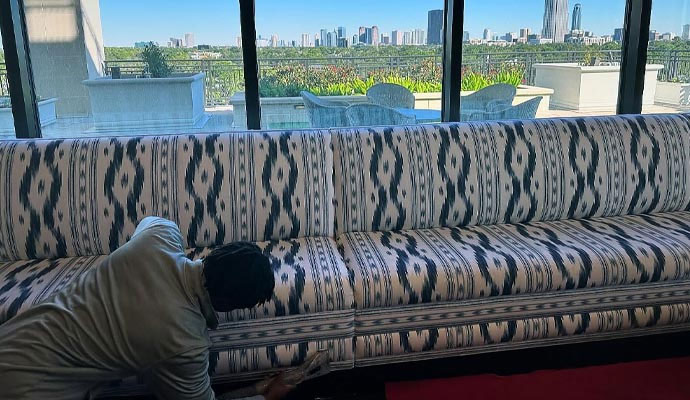Technician deep cleaning a patterned sofa in a high-rise building with a view of the Houston skyline.